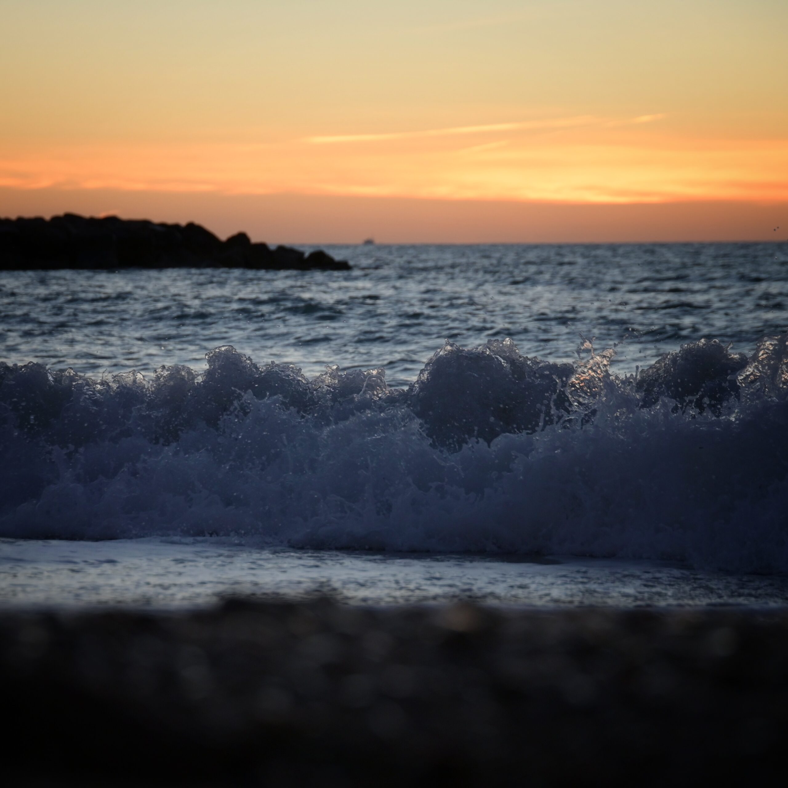 Das Meer in der Abendsonne, im Vordergrund eine hohe Welle, im Hintergrund eine Insel