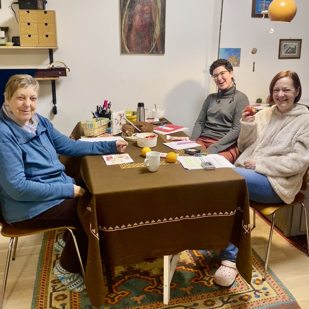 Erna, Christina und Eva sitzen in einem Wohnzimmer um einen Tisch, an dem sie gerade den Podcast aufgenommen haben.