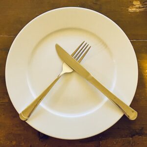 Ein leerer weißer Essteller mit darauf gekreuztem Besteck, Symbol für Fasten