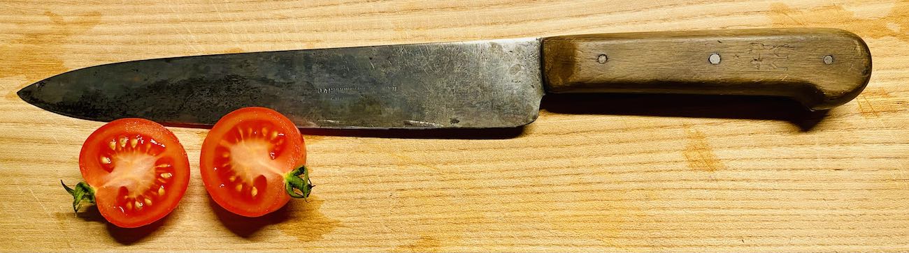 ein küchenmesser auf einem brett mit 2 paradeiserhälften