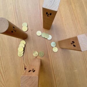 Die Holzklötze mit vier, zwei und zwei Geldstücken, die Spielleitung hat viele Geldstücke