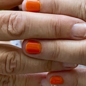 Finger bei Beuty-Behandlung mit teils orangen, teils naturfarbenen Fingernägeln