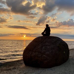 Ein Mann sitzt auf einem Stein, im Hintergrund das Meer